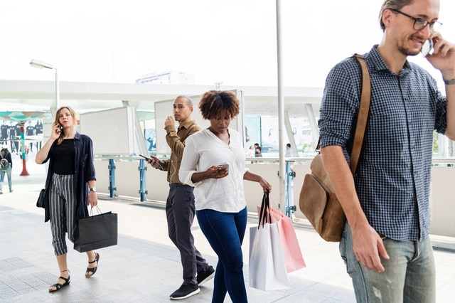Muž s koženou taškou na ramene telefonuje v obchodnom centre a okolo neho chodia ľudia s taškami.jpg